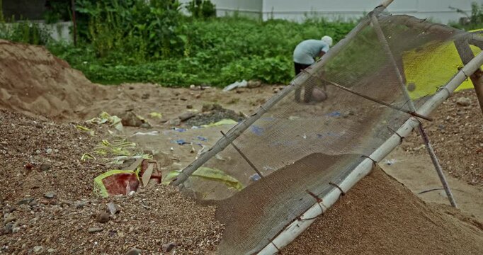 Construction Laborers Preparing Sand at an Indian Building Site Using a Handheld Metal Sieve. Skilled manual workers perform traditional sand screening work during ongoing construction activities