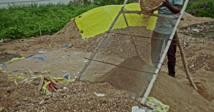 Construction Laborers Preparing Sand at an Indian Building Site Using a Handheld Metal Sieve. Skilled manual workers perform traditional sand screening work during ongoing construction activities