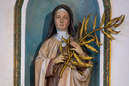 A painted statue of Saint Annette Pelras stands inside a niche holding a golden palm.