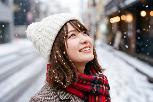雪降る街角で笑顔で空を見上げる冬服の若い女性