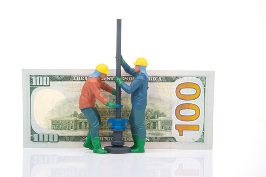 Miniature figures working together on a model drilling project with a hundred dollar bill in the background