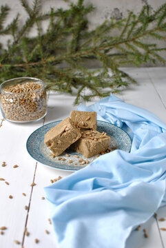 Sunflower halva pieces on a decorative plate with scattered seeds, blue fabric, a glass of kernels and evergreen branches.