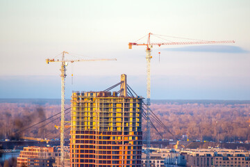 Construction activity on a high-rise building in a city with cranes in the background during sunset hours © photosaint