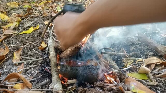 Man hands flipping and turning roasted taro on hot charcoal camp fire