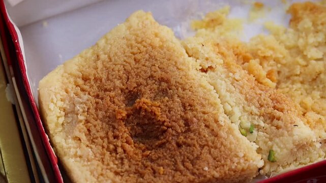 Close-up macro b-roll footage of traditional Indian sweet Milkcake or Kalakand, showcasing its rich caramelized, crumbly, and grainy texture inside a festive box.
