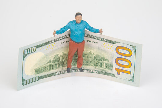 Miniature figures stand on a one hundred dollar bill in a simple setting