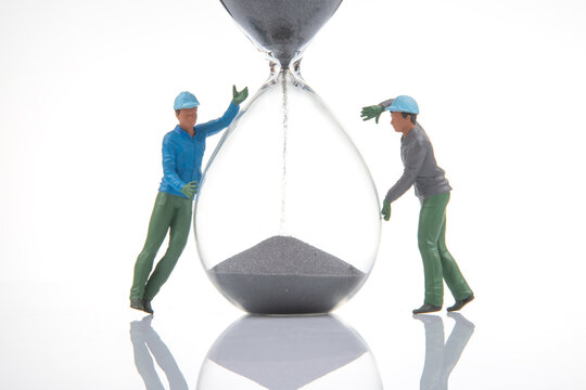 Miniature figures of workers interacting with a large hourglass in a simple scene