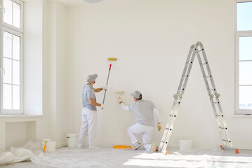 Professional wall painters renovating home interior. Two qualified male workers with buckets of white paint and paint rollers painting wall inside house or residential flat building © Studio Romantic
