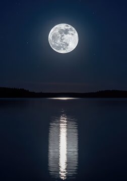 A luminous full moon glows brightly in the dark night sky, casting a shimmering silver reflection across the calm surface of a quiet lake, ripples, lake, sky