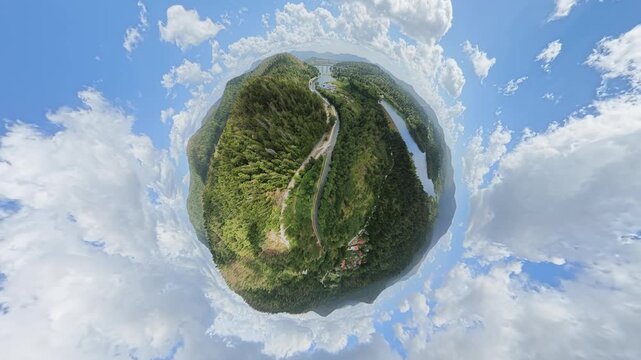 Surreal 360-degree aerial drone footage presenting a forested mountain landscape as a tiny planet surrounded by blue sky and dramatic clouds