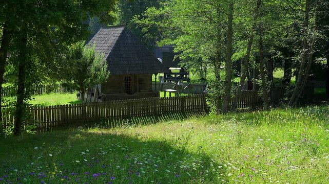 Traditional wooden house behind a picket fence in a green shaded rural setting in Romania