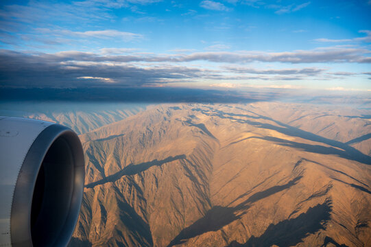 Aerial view of the Peruvian Andes during approach to Lima, Peru. Aircraft engine overlooks rugged arid mountains and deep shadows on a flight from Paris.