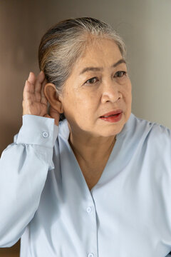 asian senior, late adult woman listening with worried expression and bad feeling, concept image for hard of hearing, hearing problem, indoor scene