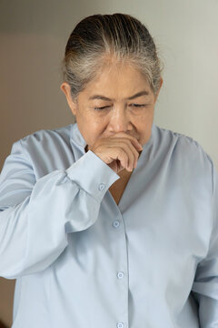 Sick and allergic old Asian senior woman suffering from runny nose, concept image for cold, flu, viral infection, dust or pollen allergy, indoor scene