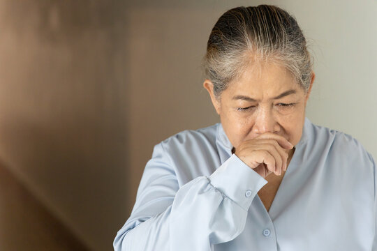Sick and allergic old Asian senior woman suffering from runny nose, concept image for cold, flu, viral infection, dust or pollen allergy, indoor scene
