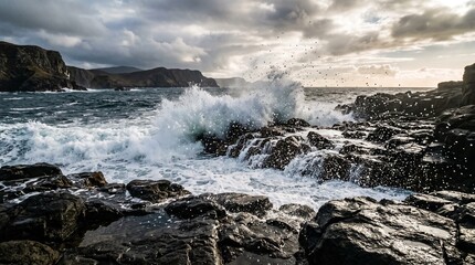 Fototapeta premium Powerful ocean waves crashing against dark jagged basalt rocks on a wild coastal shoreline under a dramatic stormy sky with breaking sunlight, majestic seascape with white sea spray and foam.