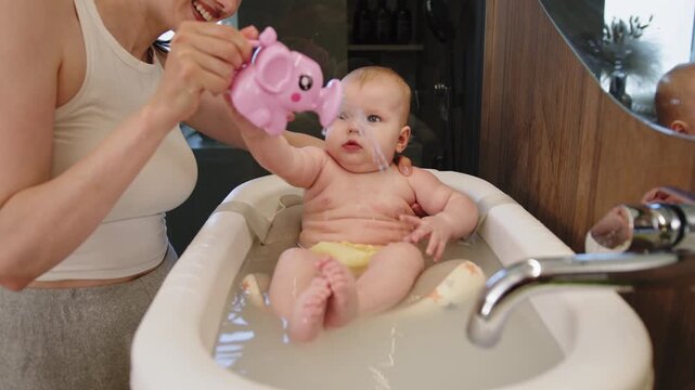 Mother washes baby in bathtub with elephant toy creating joyful moments during bath time routine. A mother bathes baby with care hygiene and joy creating family love and happiness
