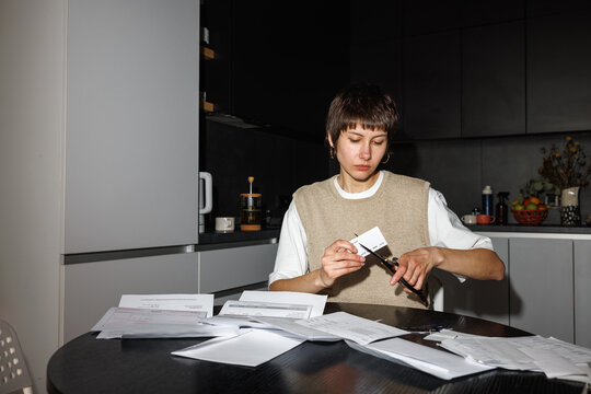 Concentrated woman cutting credit card with scissors at wooden table