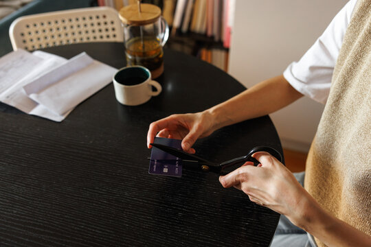 Partial side view of woman cutting credit card at desk at blurred home