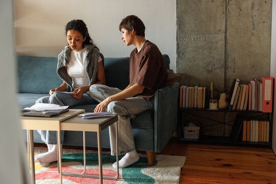 Focused woman looking at financial papers in hands of sad girlfriend