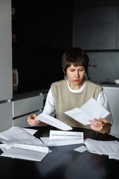 Sad and focused woman checking financial documents at desk at home