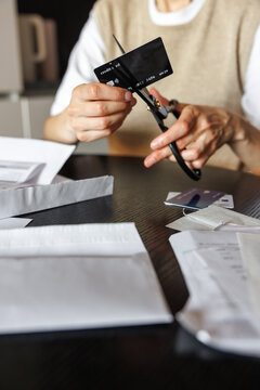 Partial view of woman cutting credit card with scissors at desk