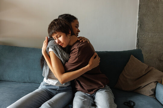 Young multiracial beautiful women hugging on sofa at home