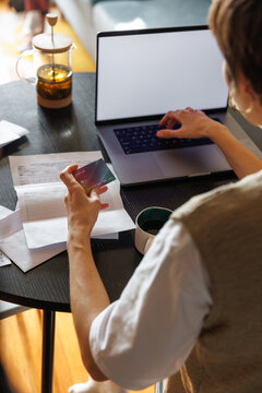 Partial back view of woman paying with credit card on laptop at desk
