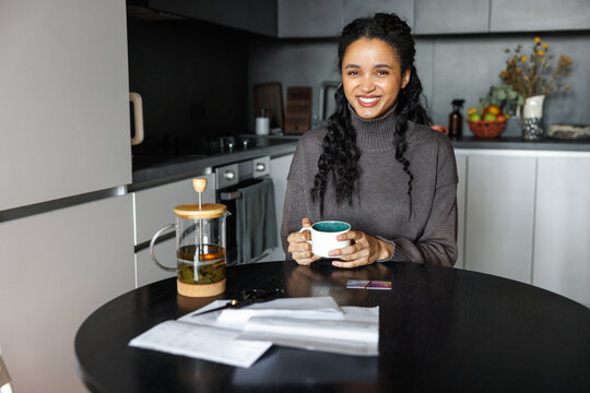 Joyful black woman drinking tea and checking financial documents