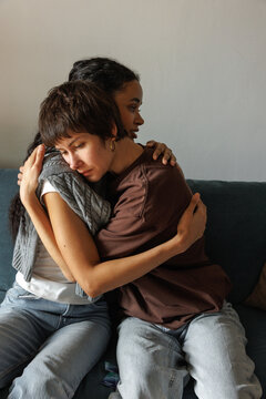 Young multiethnic pretty women embracing on couch at home