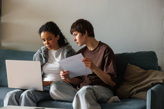 Focused multiracial women checking financial documents with laptop