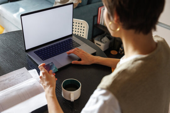 High angle of partial woman paying with credit card on laptop at desk