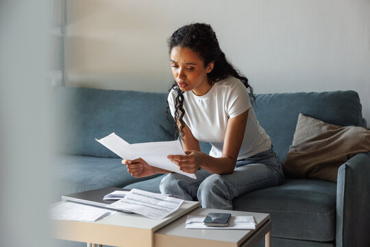 Young focused and dissatisfied black woman checking financial papers