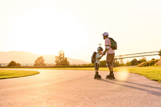 Father Holding Son's Hand While Roller Skating at Sunset