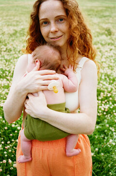 Mother holds baby in green field during daytime