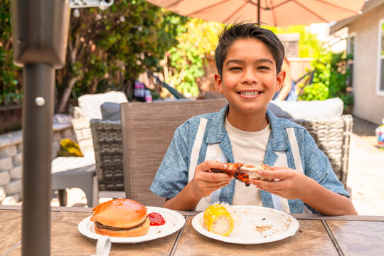 Boy smiles braces eating summer Barbecue Meal in Backyard 
