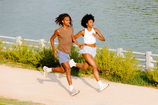Multiracial couple training as runners near a park lake at sunrise