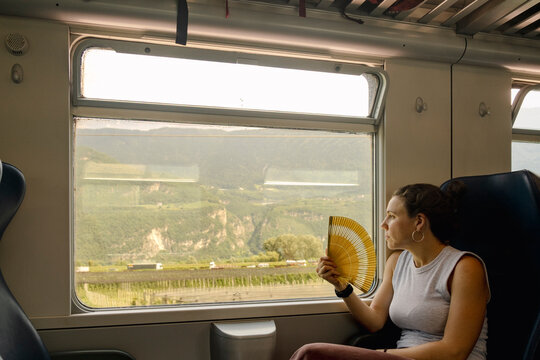 UGC Woman with fan looking out train window on summer journey