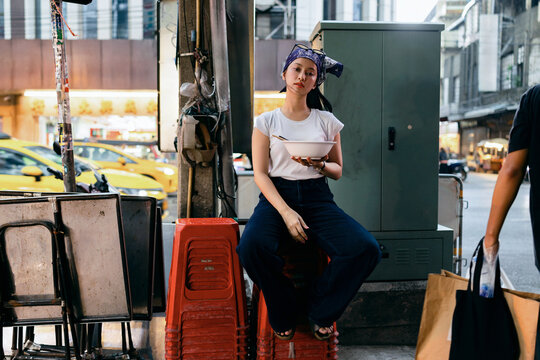 Young Woman Eating Noodles On Urban Street Corner