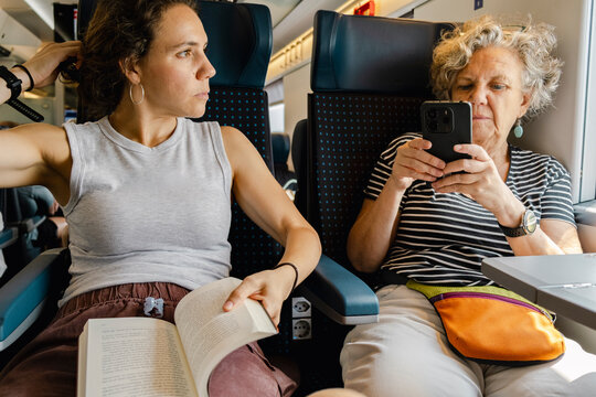 Mother using phone while daughter reads book on train