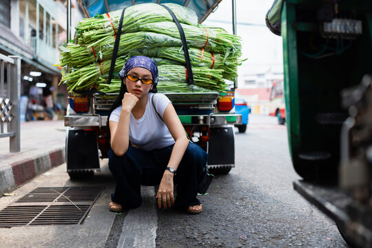 Young Woman Squatting By Vegetable Truck At Market