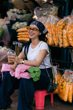 Smiling Woman Sitting at Busy Flower Market Stall