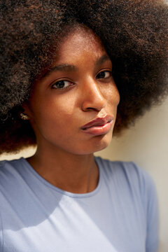 Woman With Curly Hair in Light Blue Shirt Looks at the Camera