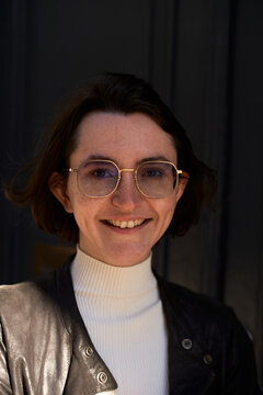 Young Person Smiling in Front of Dark Door Wearing Glasses