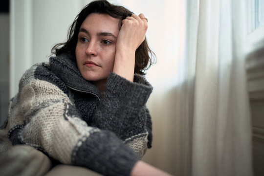 Woman Sitting by a Window With a Thoughtful Expression at Home