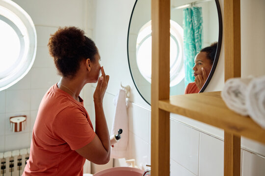 Woman tends to her skin while looking in the mirror.
