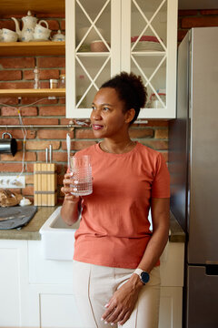 Woman stands by the fridge with a glass of water