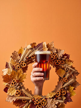 Hand holding dark beer glass through autumn leaves and pretzel wreath