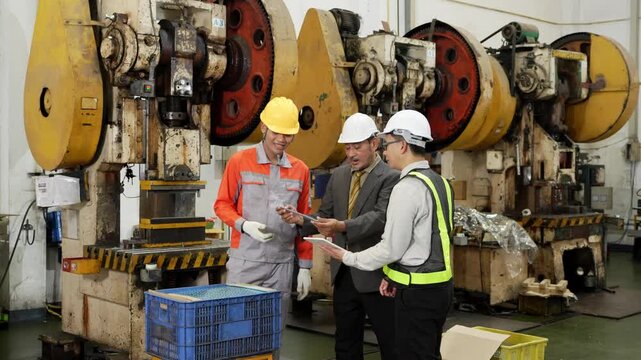 Factory audit gathers three managers around a freshly stamped metal part beside the long row of mechanical power presses