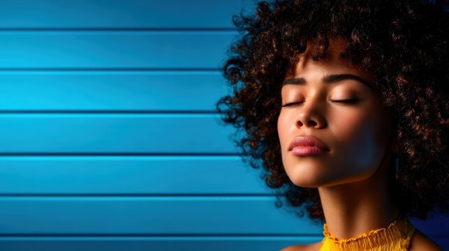 A calm and serene young woman poses against a minimalistic blue background, evoking feelings of tranquility and introspection, showcasing beauty within simplicity and style.